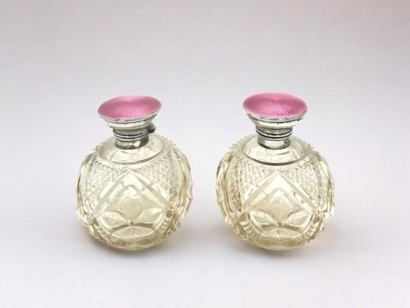 Due bottiglie da profumo in cristallo intagliato con tappi in argento e smalto Due bottiglie da profumo in cristallo intagliato con tappi in argento e smalto