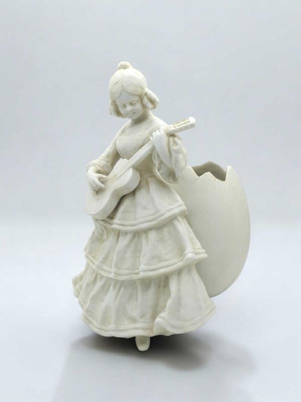 Statuetta portafiori in bisquit raffigurante una suonatrice di chitarra con dietro un grande uovo Statuetta portafiori in bisquit raffigurante una suonatrice di chitarra con dietro un grande uovo
